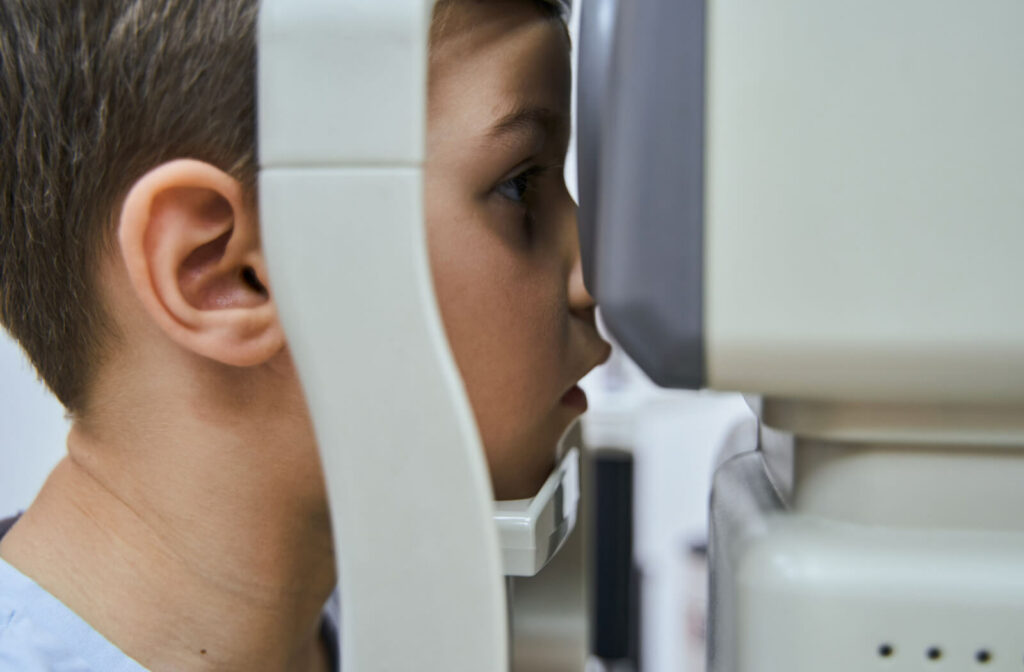 A boy patient is seated while his chin is rested in a stabilizing chinrest and focusing his eyesight on an image showing on the screen of an Autorefractor machine.