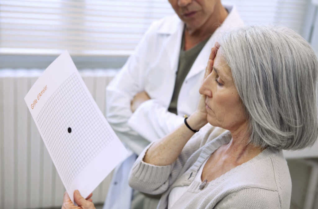An elderly woman is undergoing an Age-related macular degeneration visibility test, she's covering her right eye while looking at an Amsler Chart she's holding in her left hand.