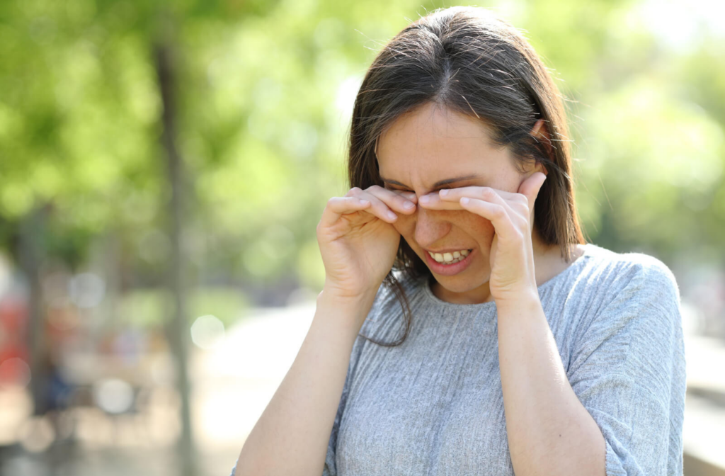 A woman in the park rubbing her eyes due to eye problems.