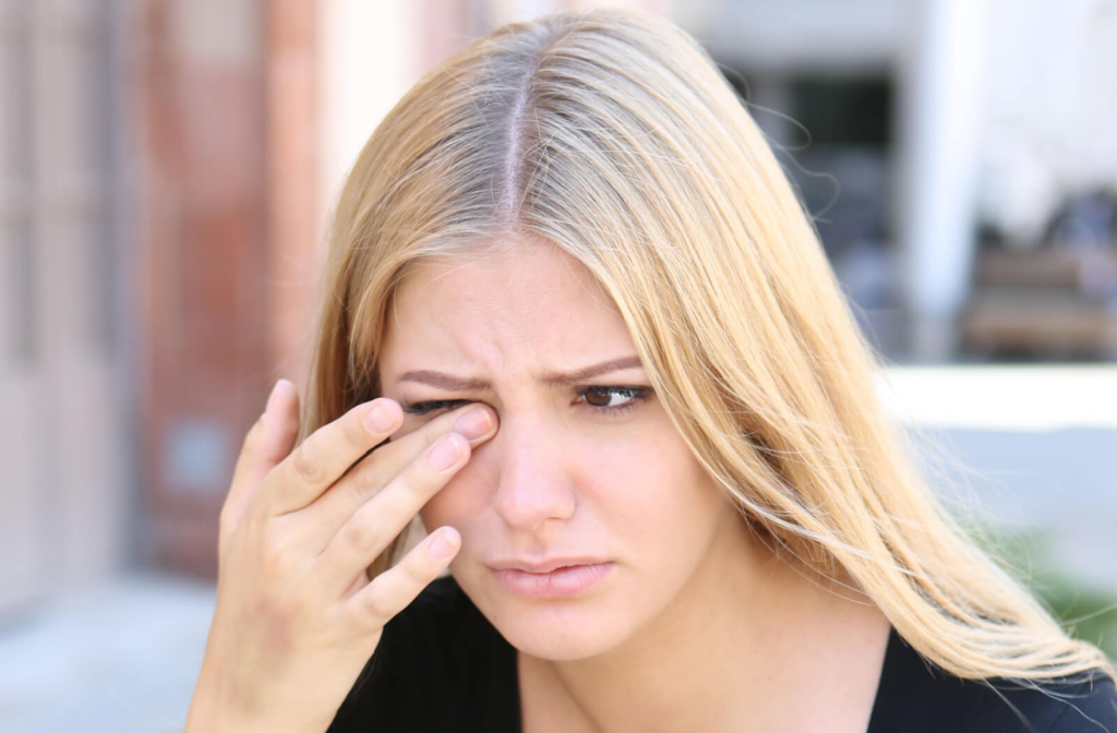 A blonde woman with a concerned look on her face rubbing her right eye with her right hand.