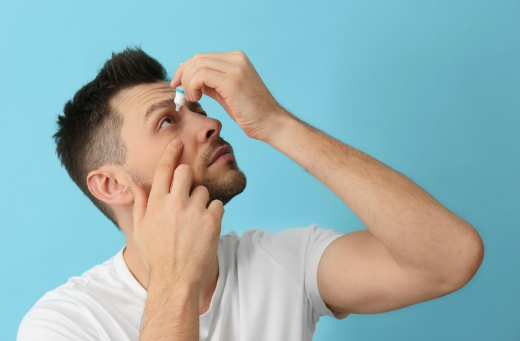 A man holding a small bottle of eye drops in his left hand and putting them on his right eye due to eye allergies.