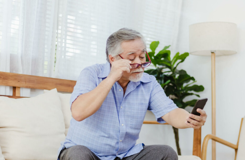 A senior man holding a smartphone at arm's length and adjusting his glasses to see clearly.
