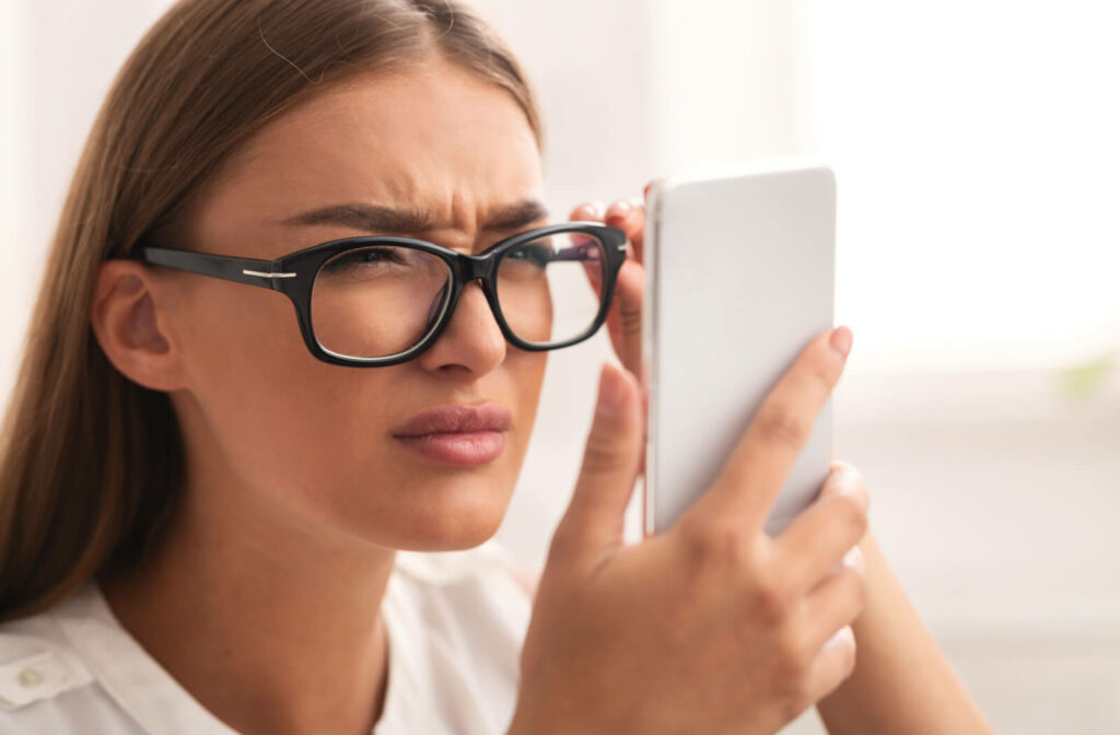 A woman with eye glasses holds her smartphone very close to her eyes.