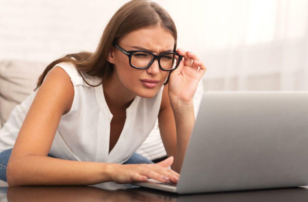 A woman holding her eyeglasses with left hand, squinting to see clearly on her laptop.