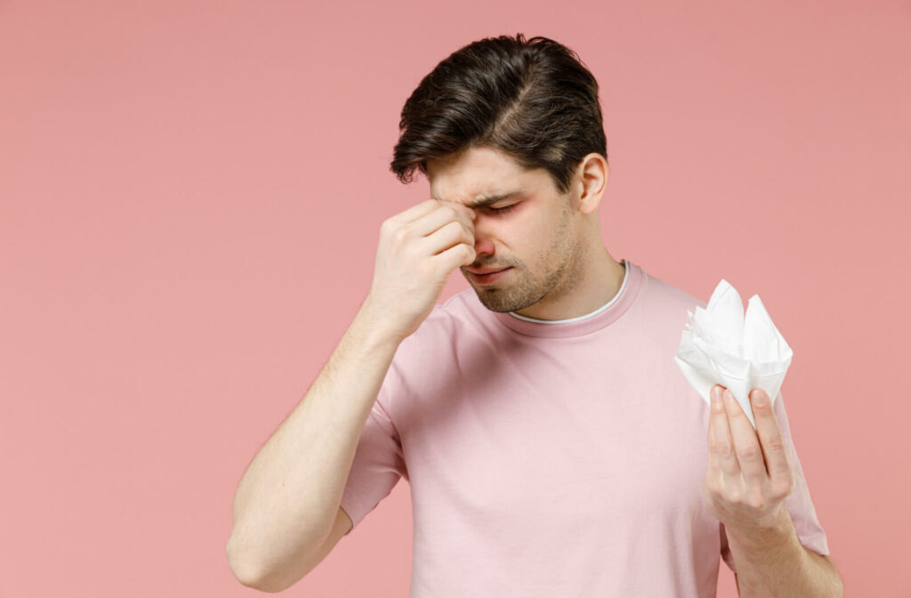 A young man with sinus problem holding tissues and pinching his nose.