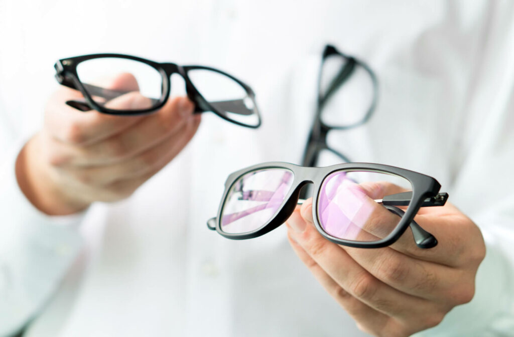 An optician holding 2 pairs of eyeglasses.