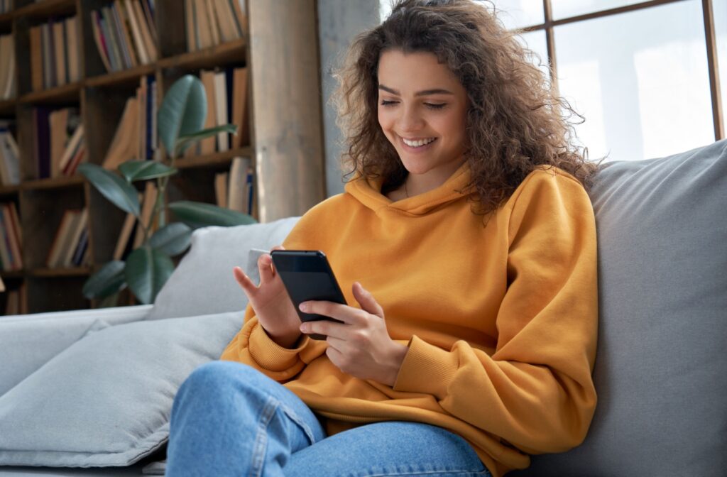 A woman sitting on a couch holding a phone that is set to dark mode on her screen