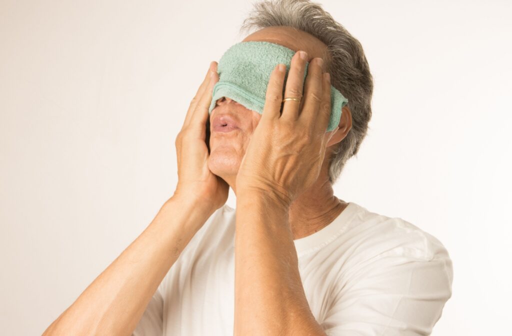 An older gentleman covers his eyes with a warm compress to alleviate dry eyes.