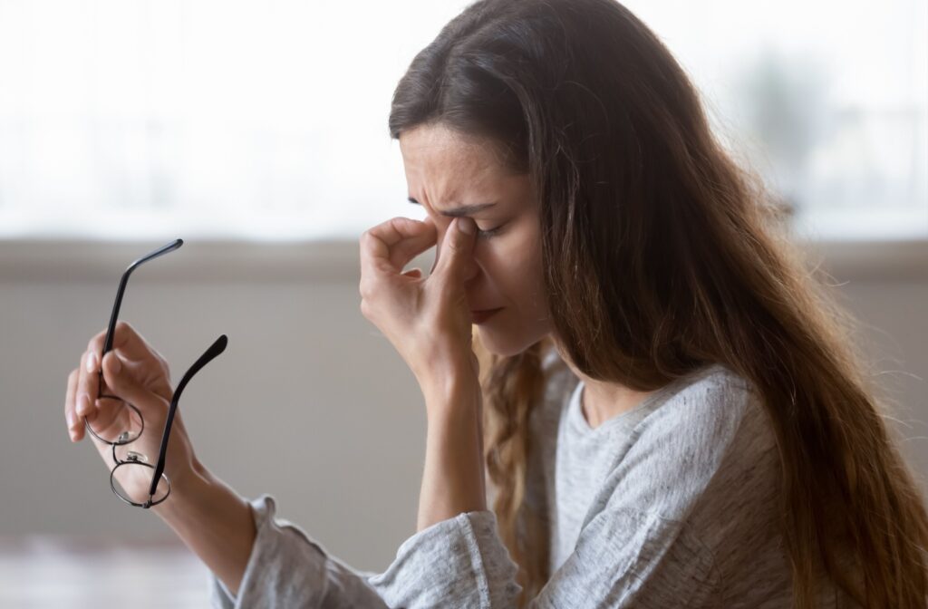 A person holding the bridge of their nose and their glasses in the other hand due to dry eye discomfort.