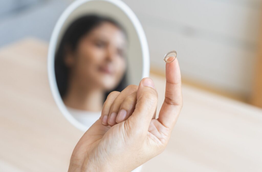 A contact lens on the tip of a person's finger, while they look in a mirror.
