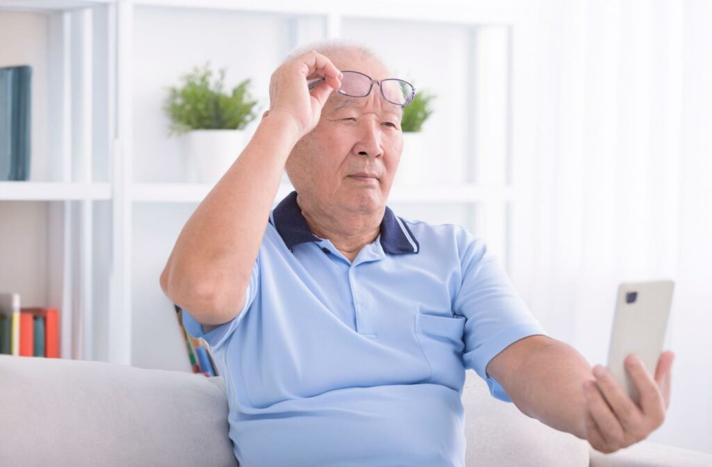A person lifting up their glasses and holding their phone out from their face to read the screen better due to presbyopia.