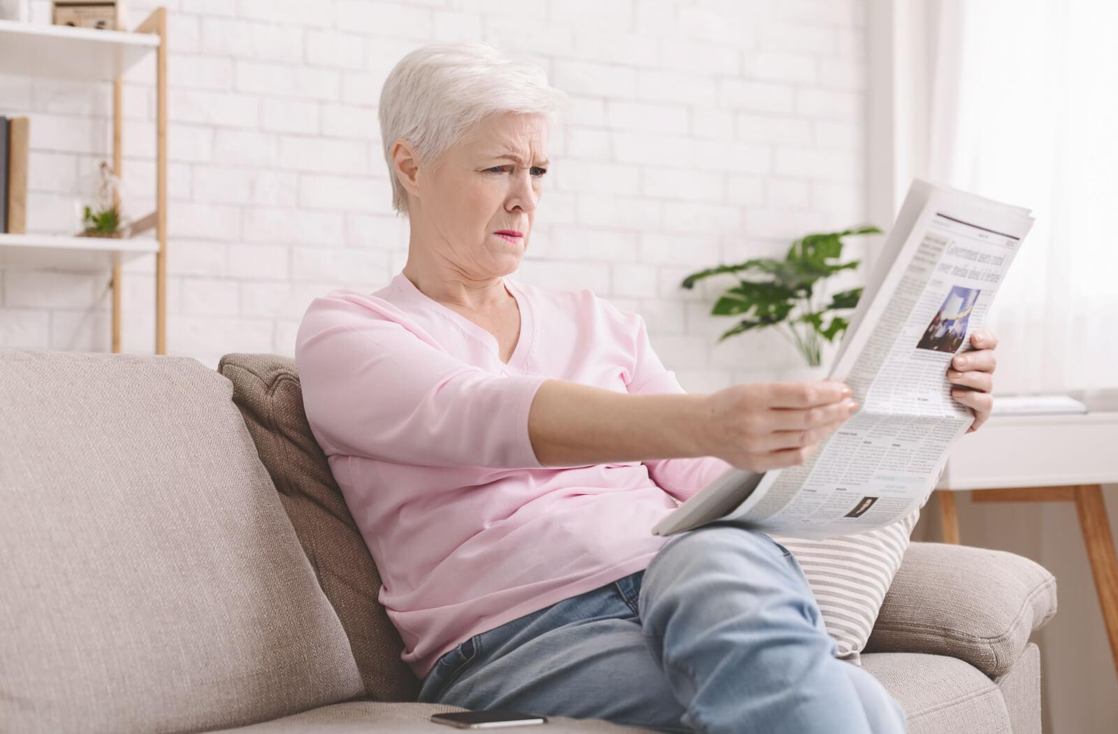 A person with presbyopia holding out a newspaper in order to read it.